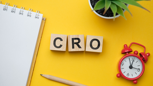 Wooden blocks C R O on a yellow background. Also in the picture is an alarm clock, pencil and writing pad.